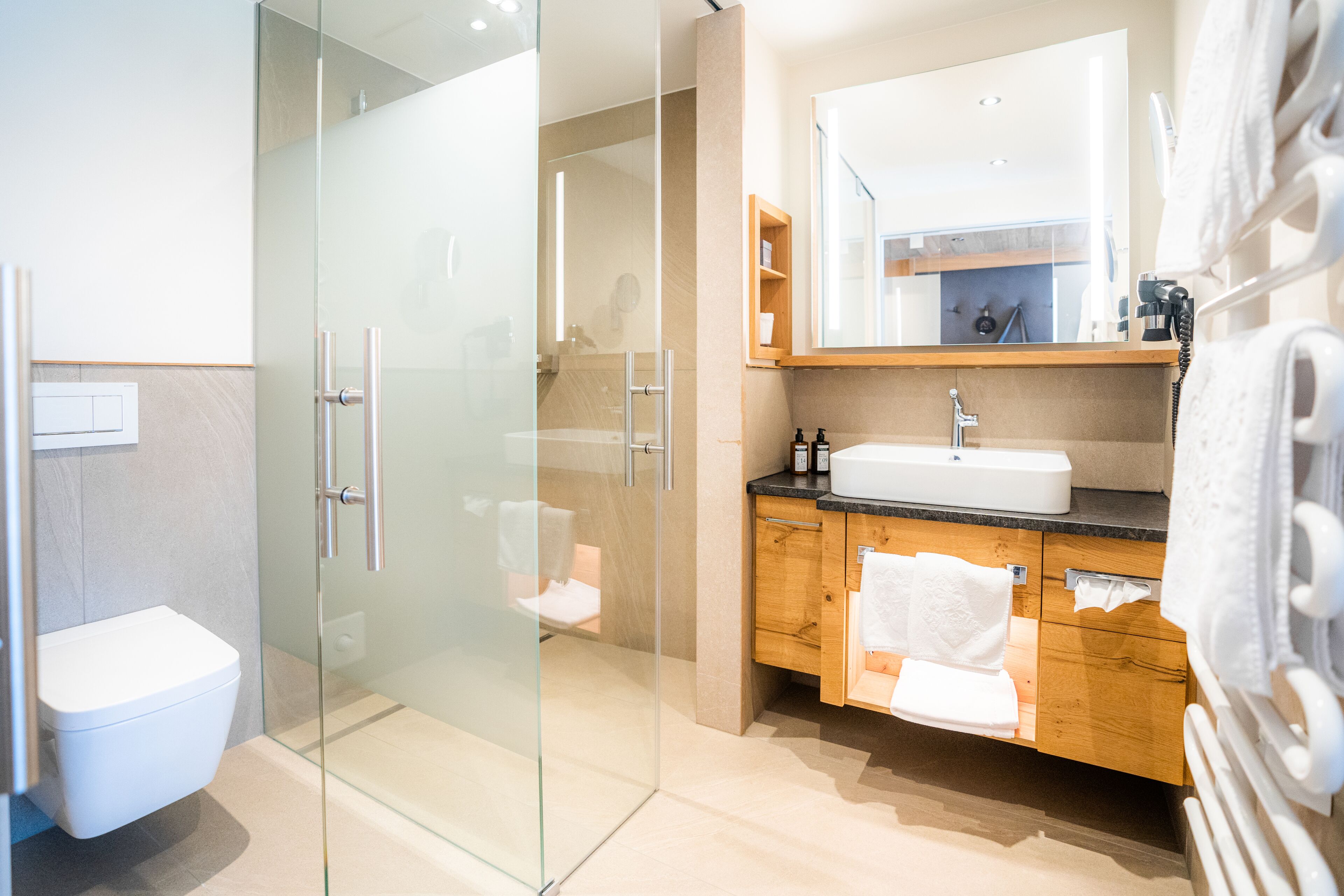 Un baño moderno con cabina de ducha de vidrio, inodoro blanco, tocador de madera con lavabo y espejo sobre el tocador.