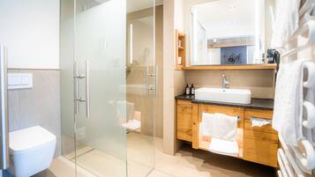 Un baño moderno con cabina de ducha de vidrio, inodoro blanco, tocador de madera con lavabo y espejo sobre el tocador.