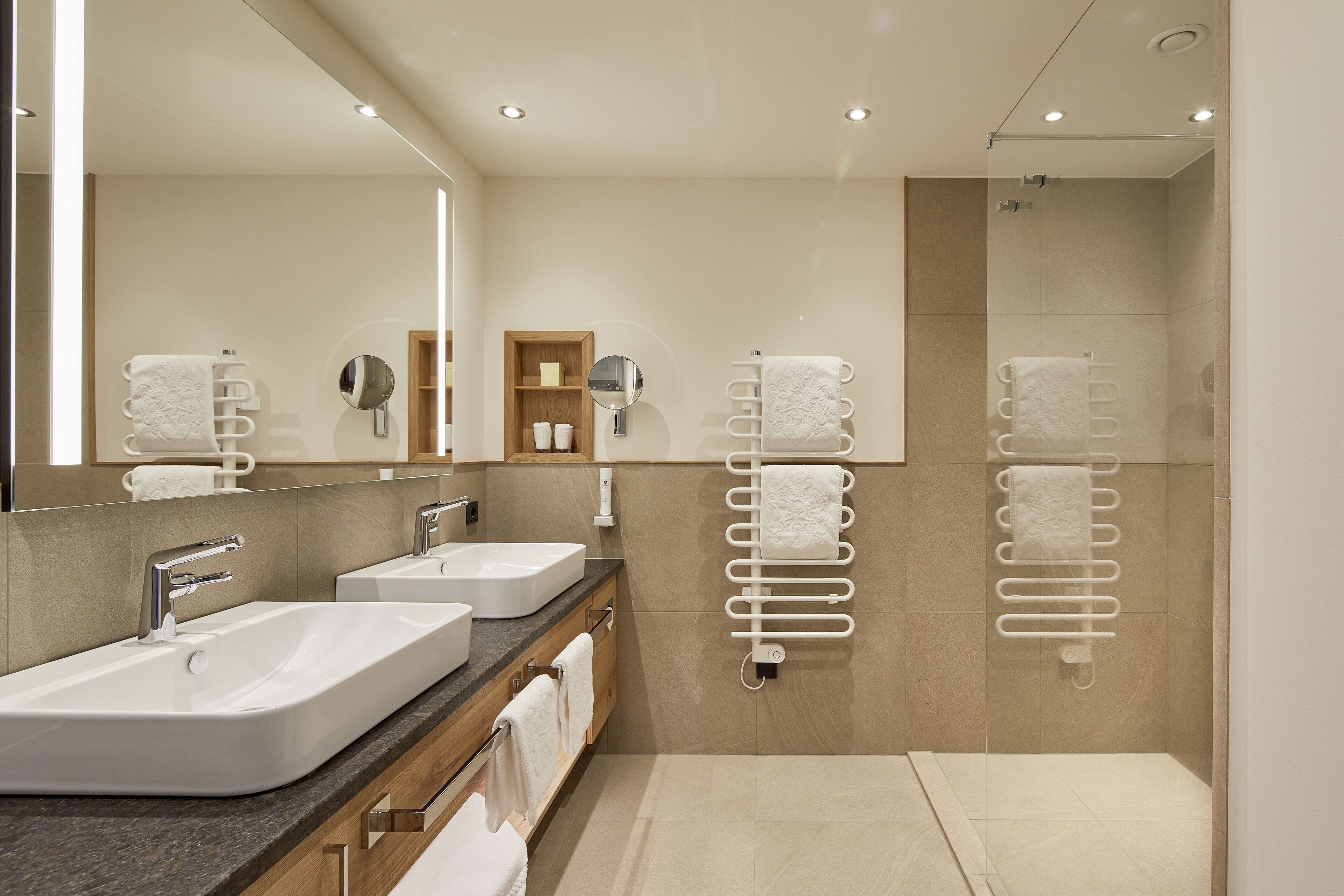 A modern bathroom with two sinks, a large mirror, and towel racks.