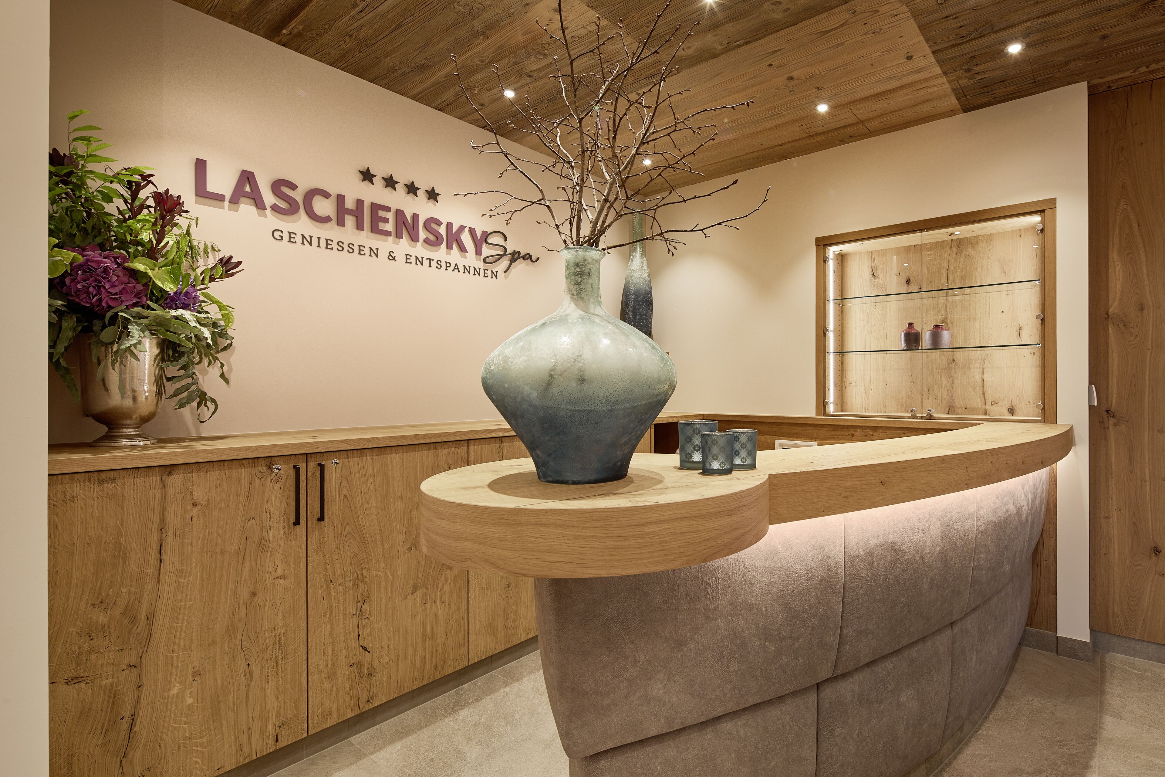 A reception desk with a vase of branches, a wooden cabinet, and a wall with the name "LASCHENSKY Spa".