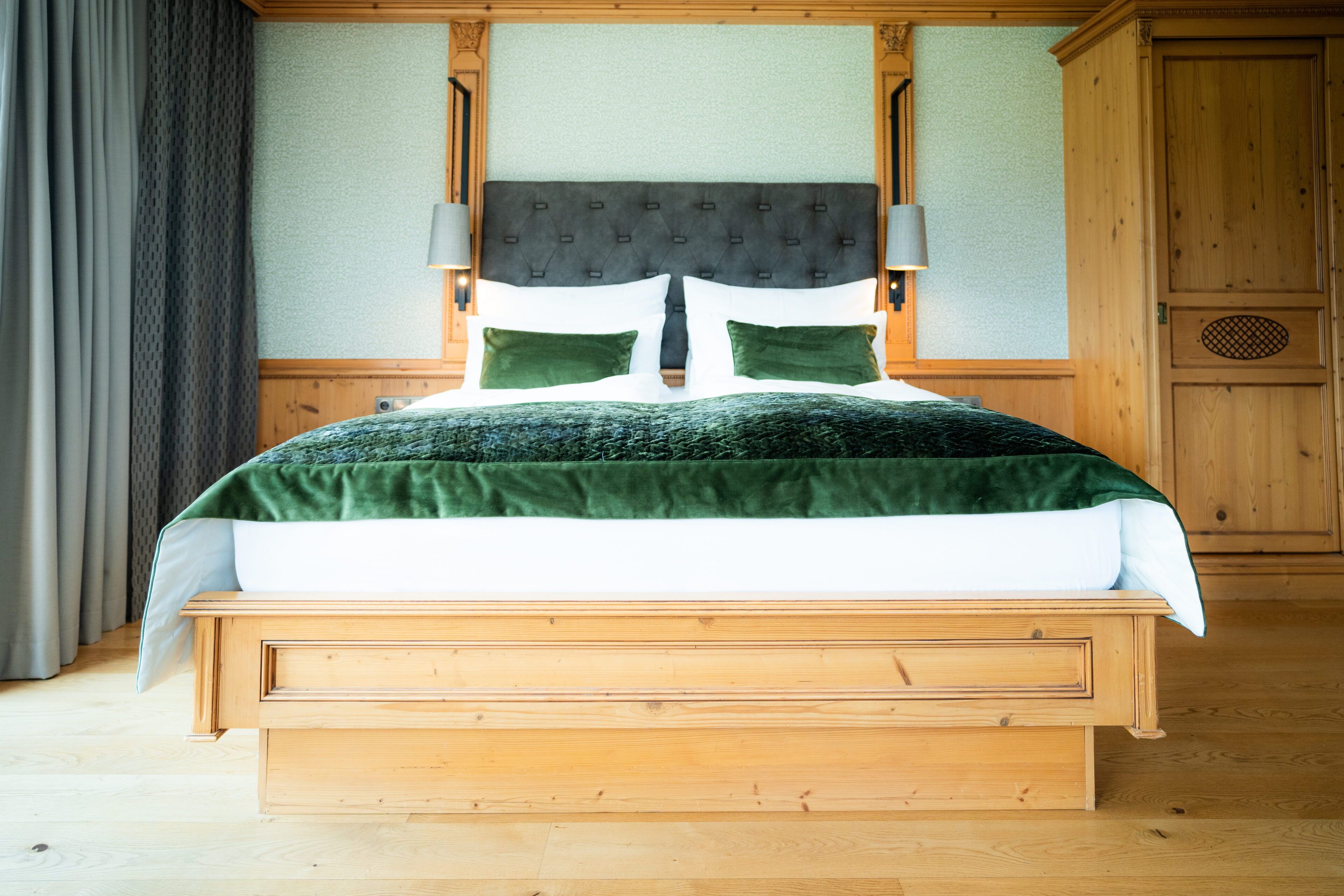 A wooden bed with a green and white bedspread, two green pillows, and a headboard with a tufted design.
