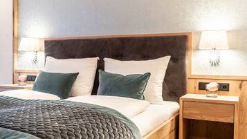 Una cama bien hecha con un cabecero oscuro, dos lámparas de noche y una mesita de madera con un florero.