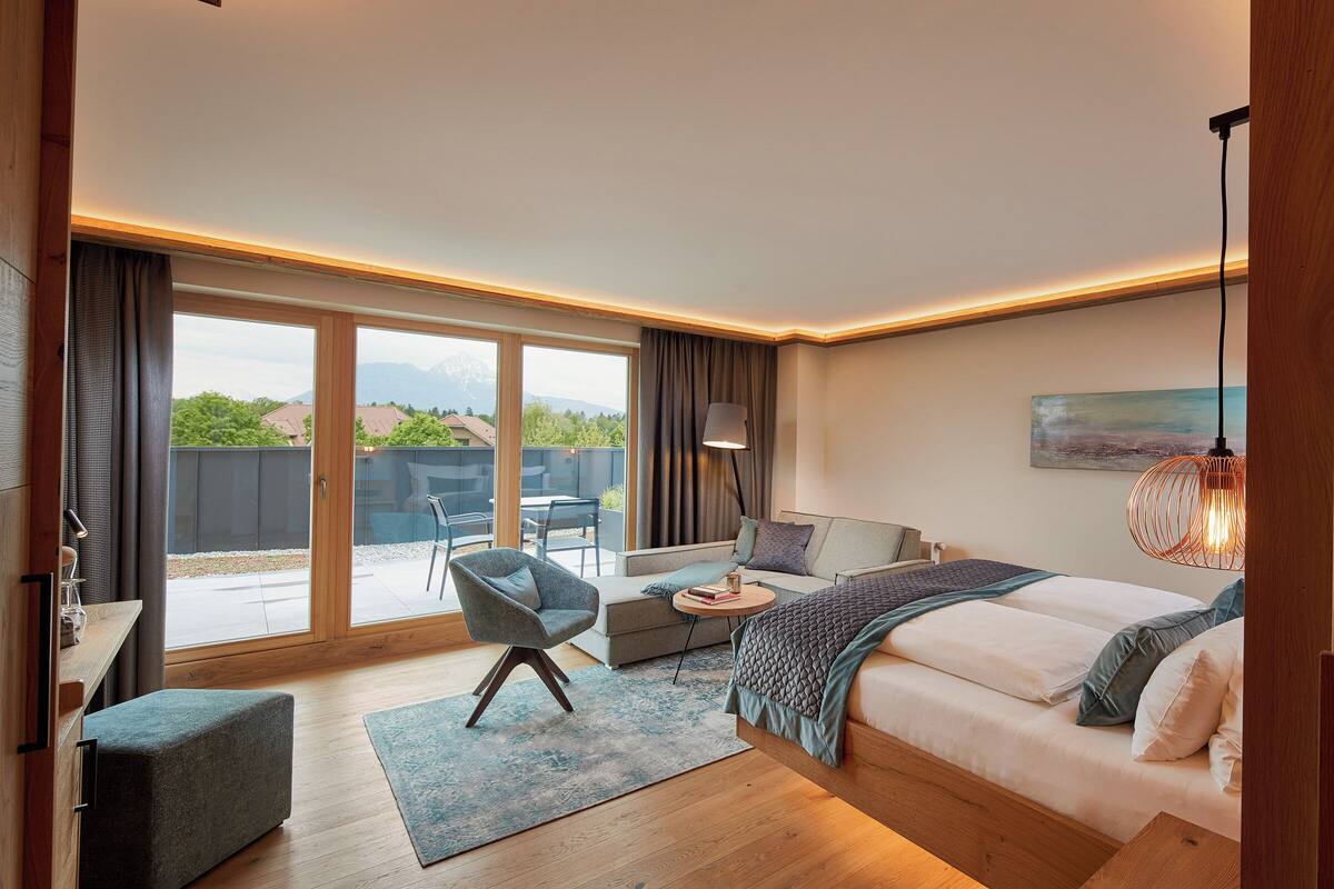 Un dormitorio moderno con una cama grande, un sofá, una silla y una mesa de comedor. Hay una ventana amplia con vistas al exterior.