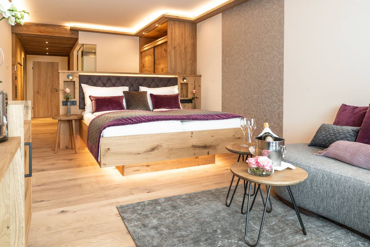 Un dormitorio moderno con una cama de madera, un sofá gris y una pequeña mesa redonda con un florero.