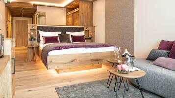 A modern bedroom with a wooden bed, a grey sofa, and a small round table with a vase of flowers.