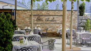 An outdoor patio with stone walls, tables, and chairs, featuring a mountain view.