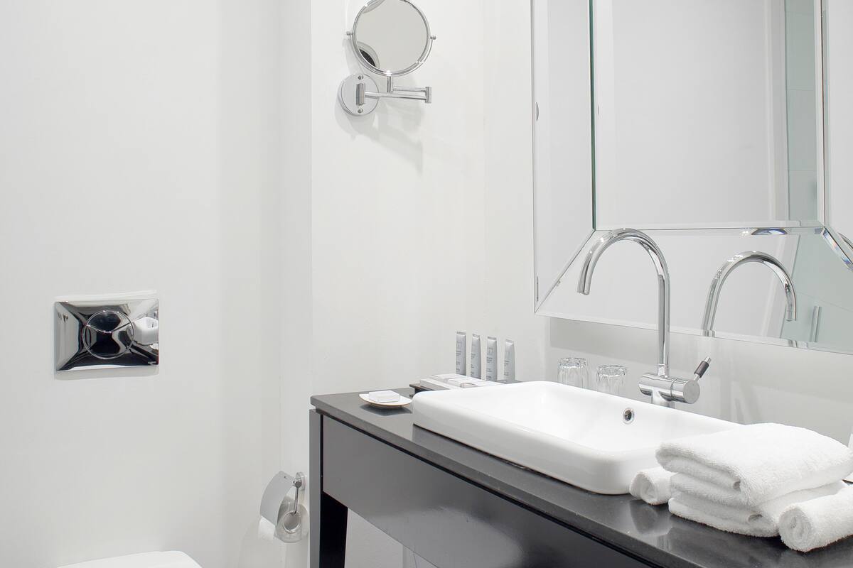 Une salle de bain moderne avec des toilettes blanches, une douche en verre, un lavabo avec un miroir au-dessus et un porte-serviettes.