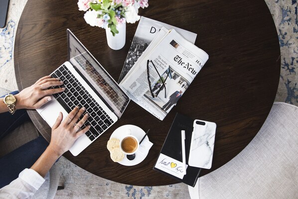 A laptop on a round table with a newspaper, a cup of coffee, and a smartphone.