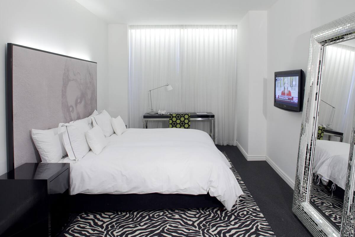 Une chambre d’hôtel avec un grand lit, un bureau, une chaise, une télévision et un miroir.