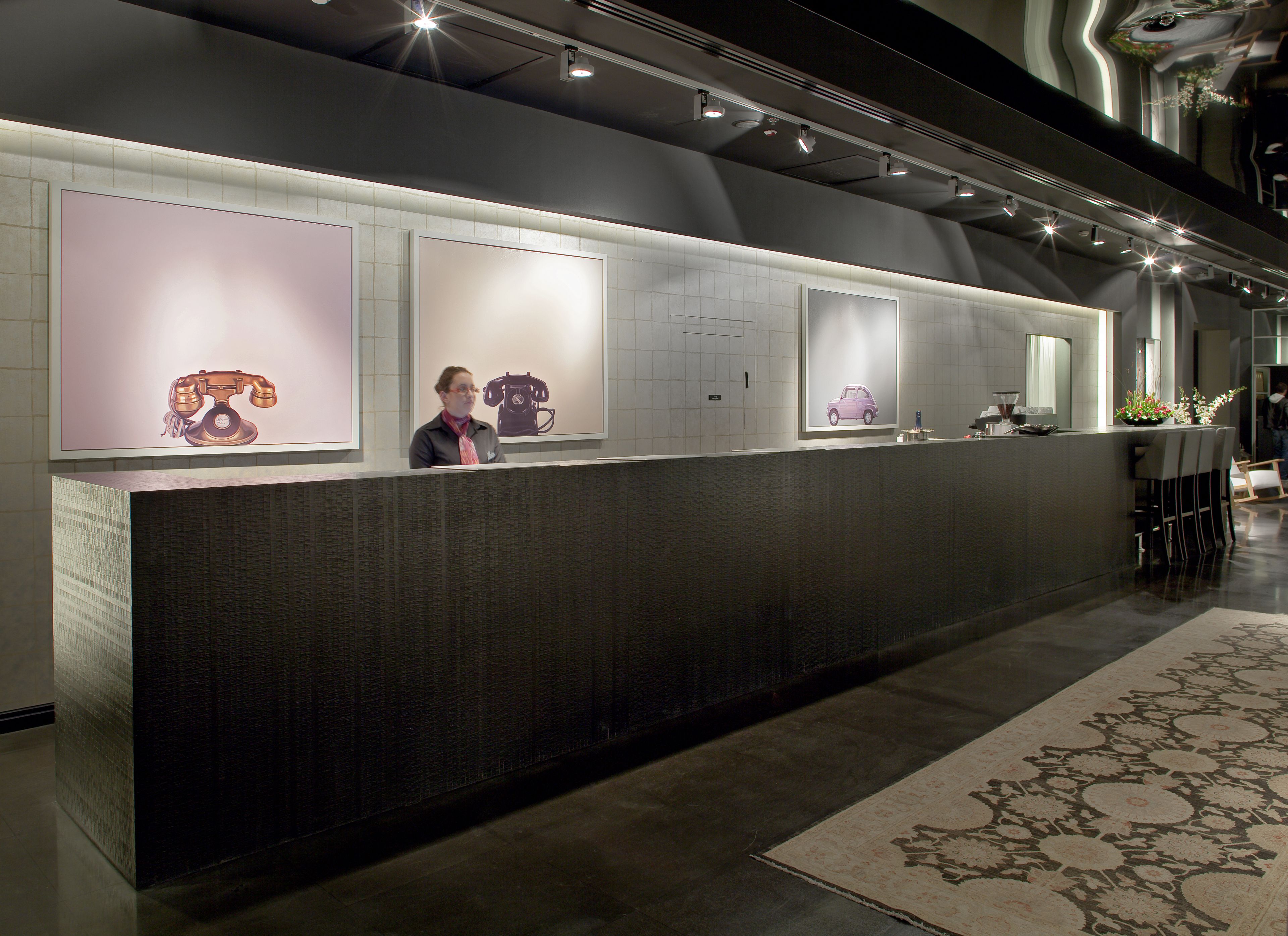 A reception area with a counter, a person standing behind it, and three framed pictures on the wall.
