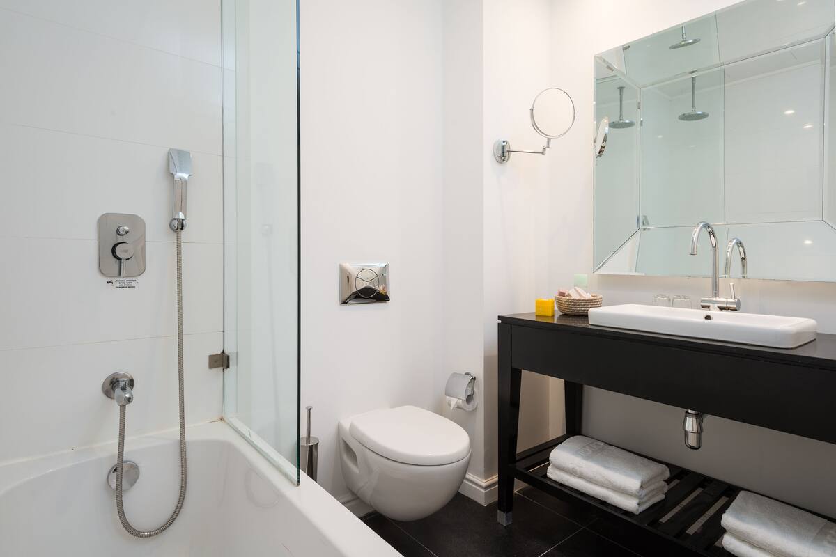 Une salle de bain moderne avec une douche à parois de verre, des toilettes blanches, un meuble-lavabo noir avec un miroir et un lavabo blanc.