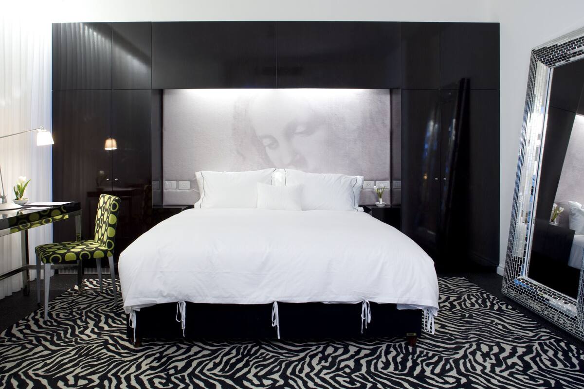 Une chambre d’hôtel moderne avec un grand lit, une moquette à motifs zébrés, un bureau avec une chaise et un grand miroir.