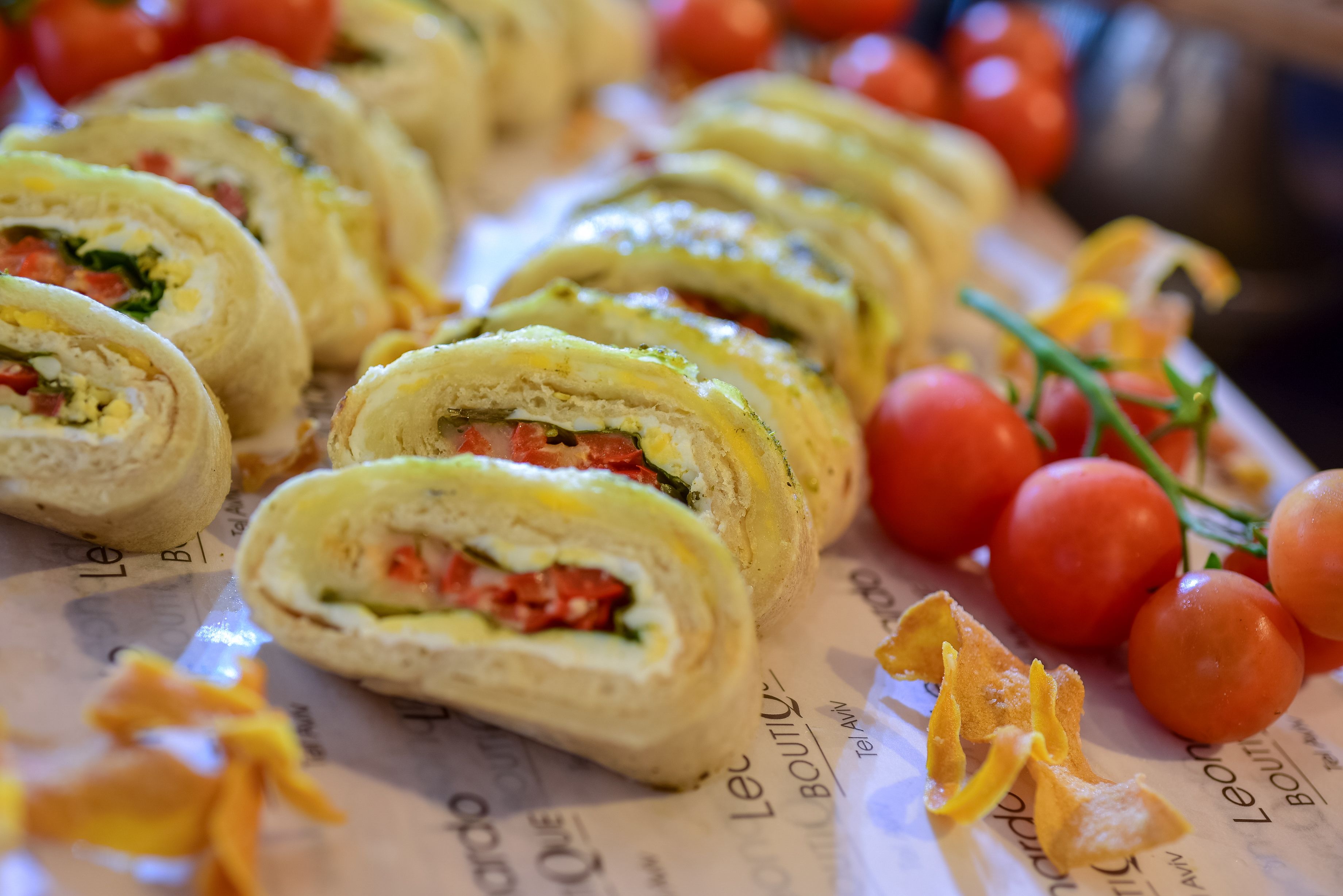 Rolled sandwiches with visible fillings, arranged on a surface with some cherry tomatoes and orange zest.