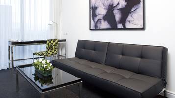 A modern living room with a glass coffee table, a patterned armchair, a grey sofa, and a large abstract painting on the wall.