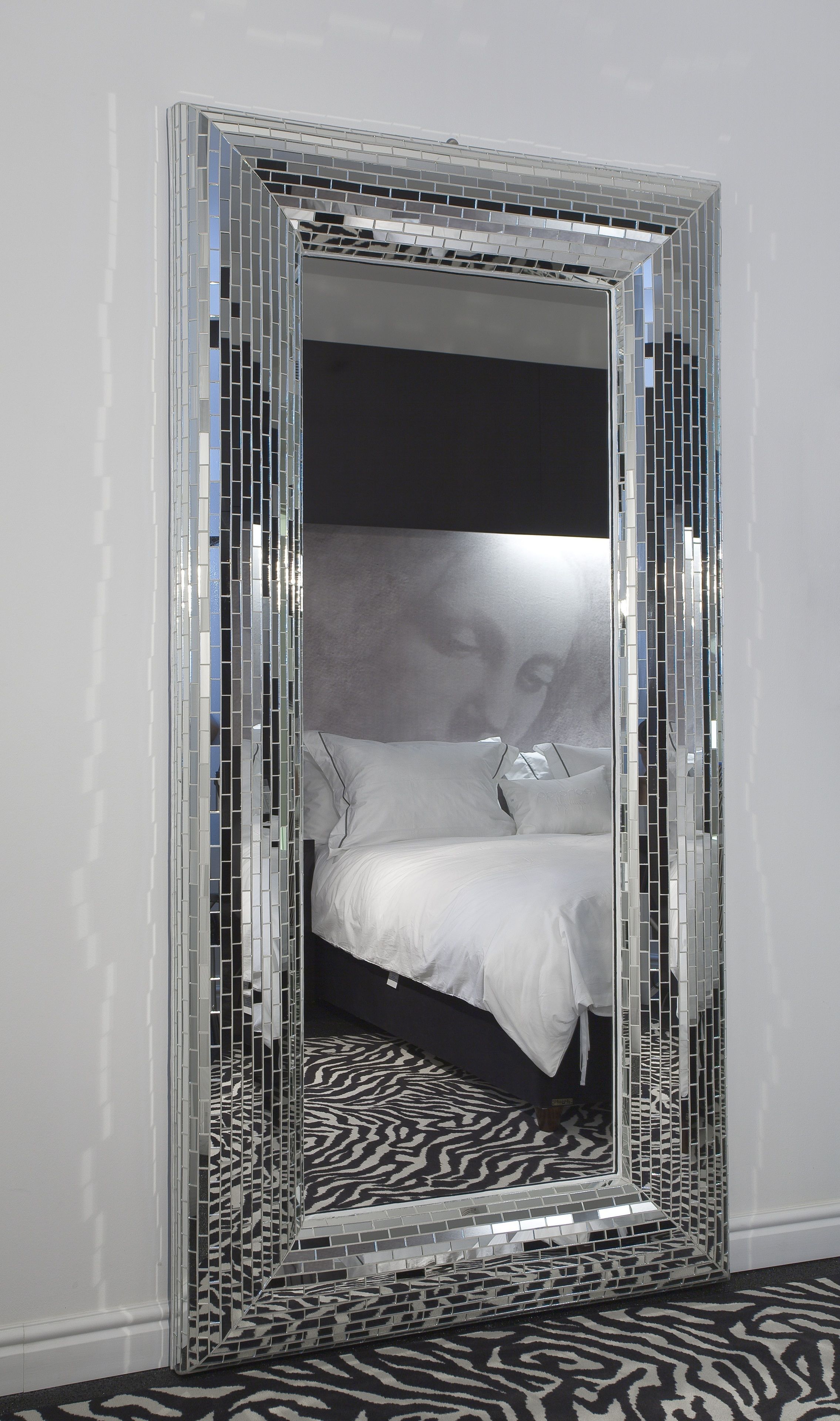 A room with a mirrored wardrobe, a bed with white bedding, and a zebra-patterned rug.