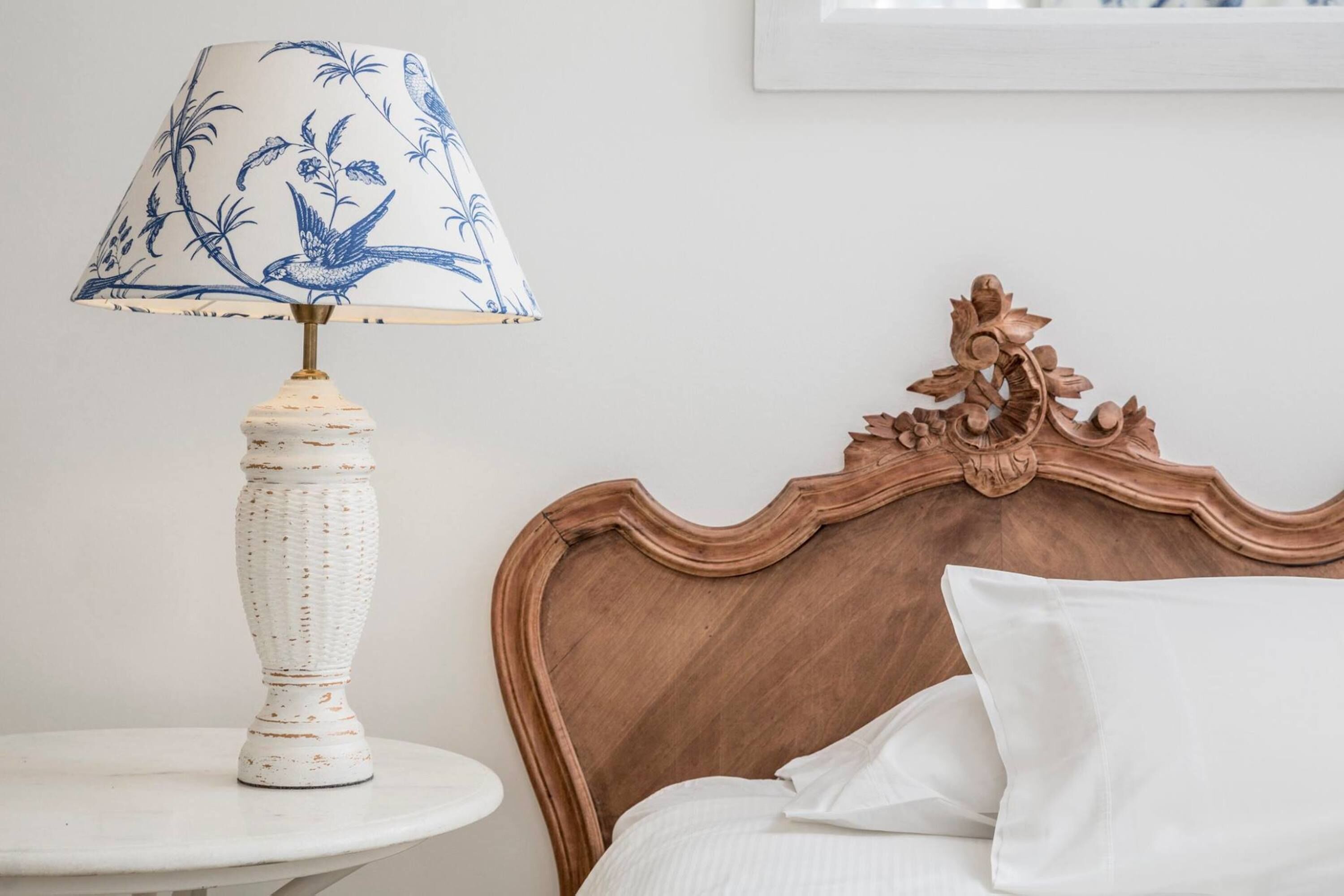 Una cama con cabecera de madera, almohada blanca y una mesita de noche con lámpara.