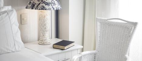 A hotel room with a bed, a nightstand with a lamp, a book, and a wicker chair.