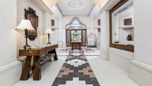 A hallway with a checkered floor, a wooden bench, and a table with lamps.