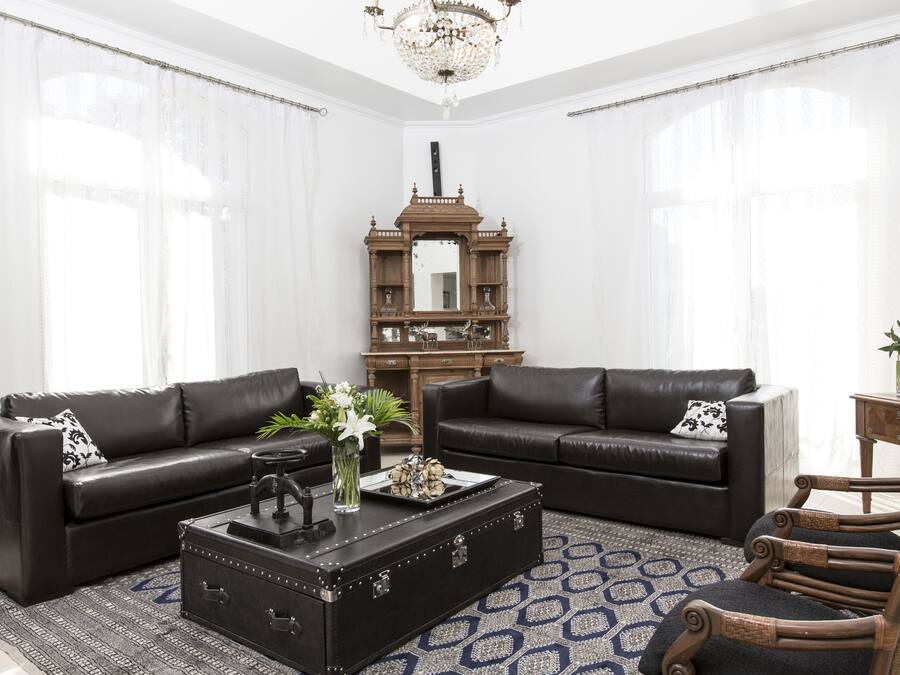 A living room with two black leather sofas, a wooden coffee table, and a wicker armchair.