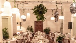A banquet hall with round tables, wooden chairs, hanging plants, and pendant lights.