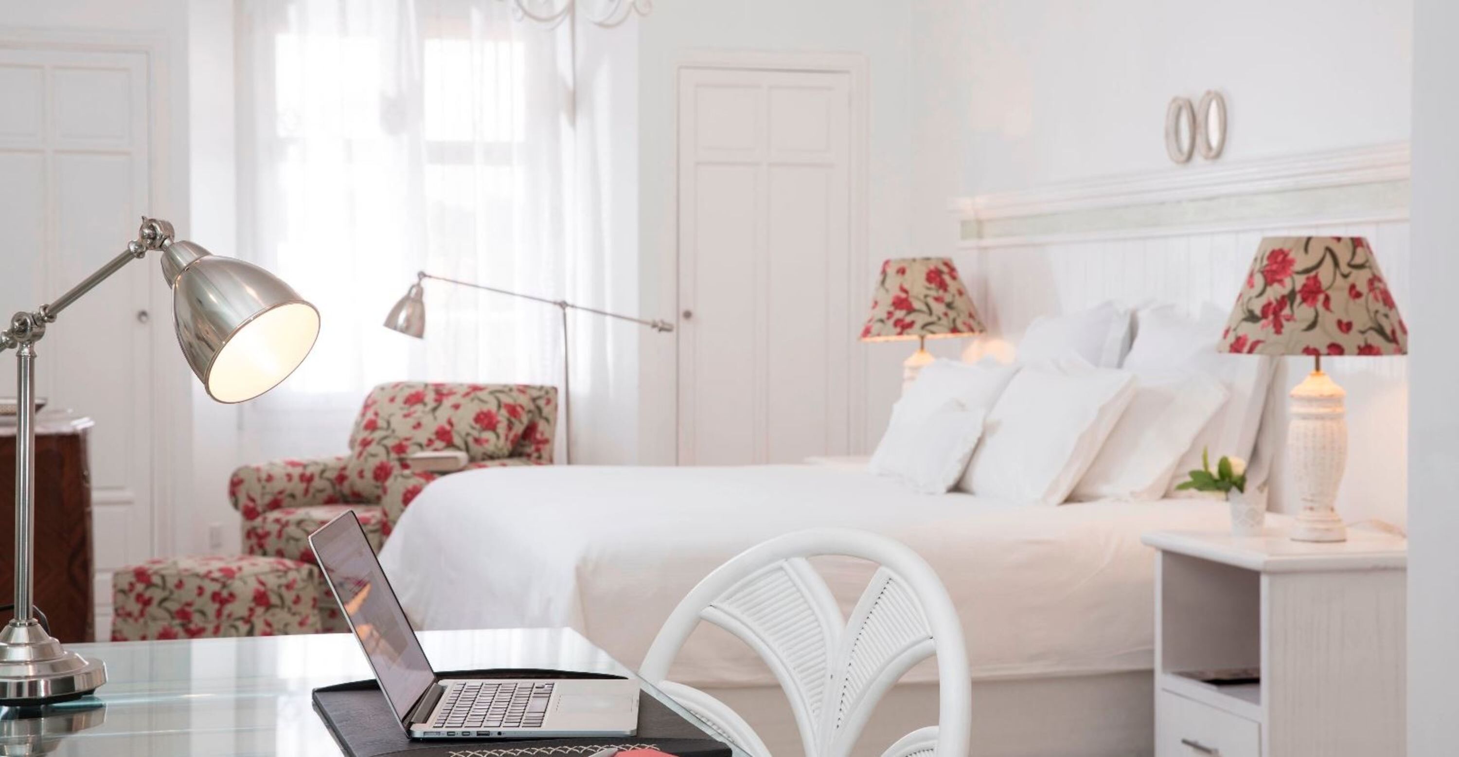 Ein Hotelzimmer mit einem Bett, einem Schreibtisch mit einem Laptop, einem Sessel und zwei Lampen.