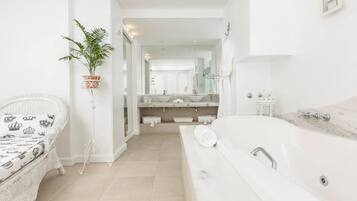 A modern bathroom with a large bathtub, a white wicker chair, a potted plant, and a vanity with a mirror.