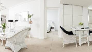 A bright, white-walled room with wicker furniture, a dining table, and a kitchen area with a microwave.