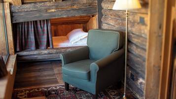Une chambre chaleureuse dans un chalet en rondins, avec un lit simple, un fauteuil vert, un tapis à motifs et une lampe.