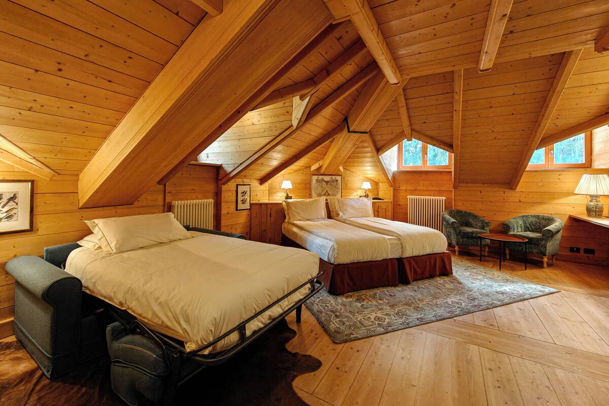 A cozy attic bedroom with two beds, a chair, and a small table.
