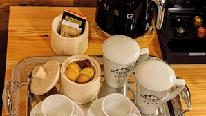 Ein Tablett mit einer Kaffeemaschine, Zuckerportionen, einer Keksdose und zwei Tassen mit Untertassen.