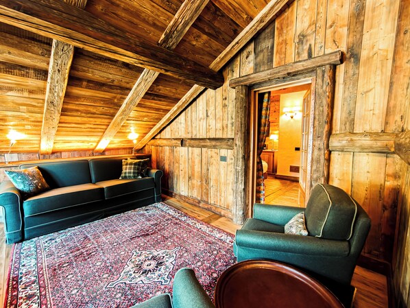 Una habitación acogedora con paredes de madera y techo inclinado, que incluye un sofá, una silla y una alfombra estampada.