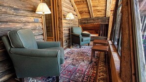 Ein gemütliches Blockhaus-Interieur mit einem grünen Sessel, einem blauen Sessel, einem kleinen Tisch und einem gemusterten Teppich.