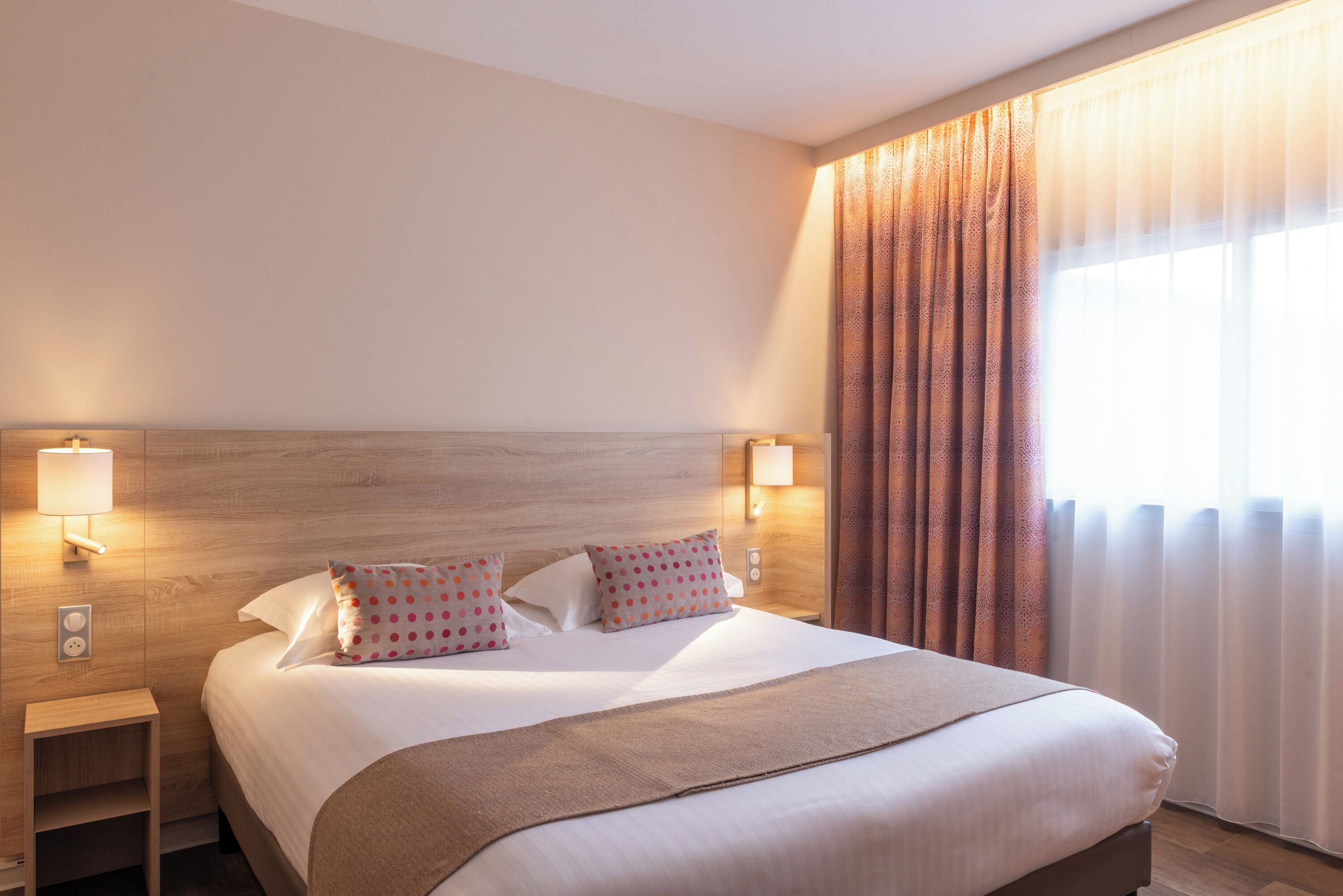 Een hotelkamer met een groot bed, twee bedlampen en een raam met gordijnen.