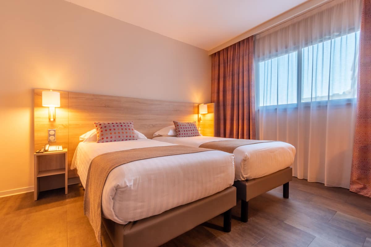 Una cama doble con cabecera de madera, dos mesitas de noche con lámparas y un ventanal con cortinas.