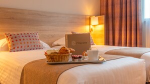 Camera d'albergo con due letti, un vassoio per la colazione con croissant, una tazza di caffè e un cestino di pane.