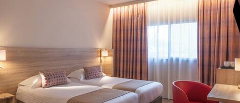 A hotel room with two beds, a desk, and a chair.