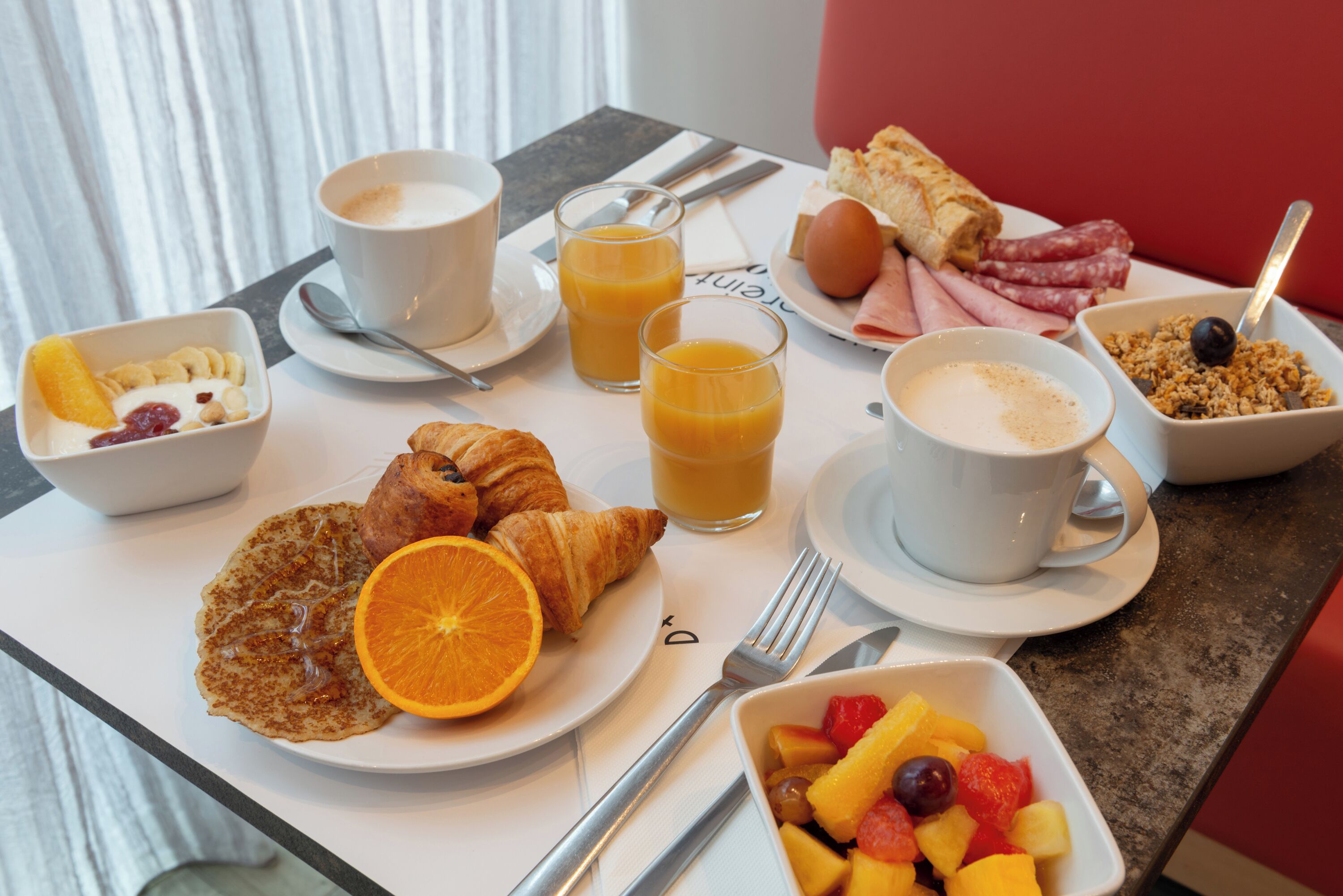 Ein Frühstückstisch mit Croissants, Orangensaft, Kaffee und einer Obstschale.