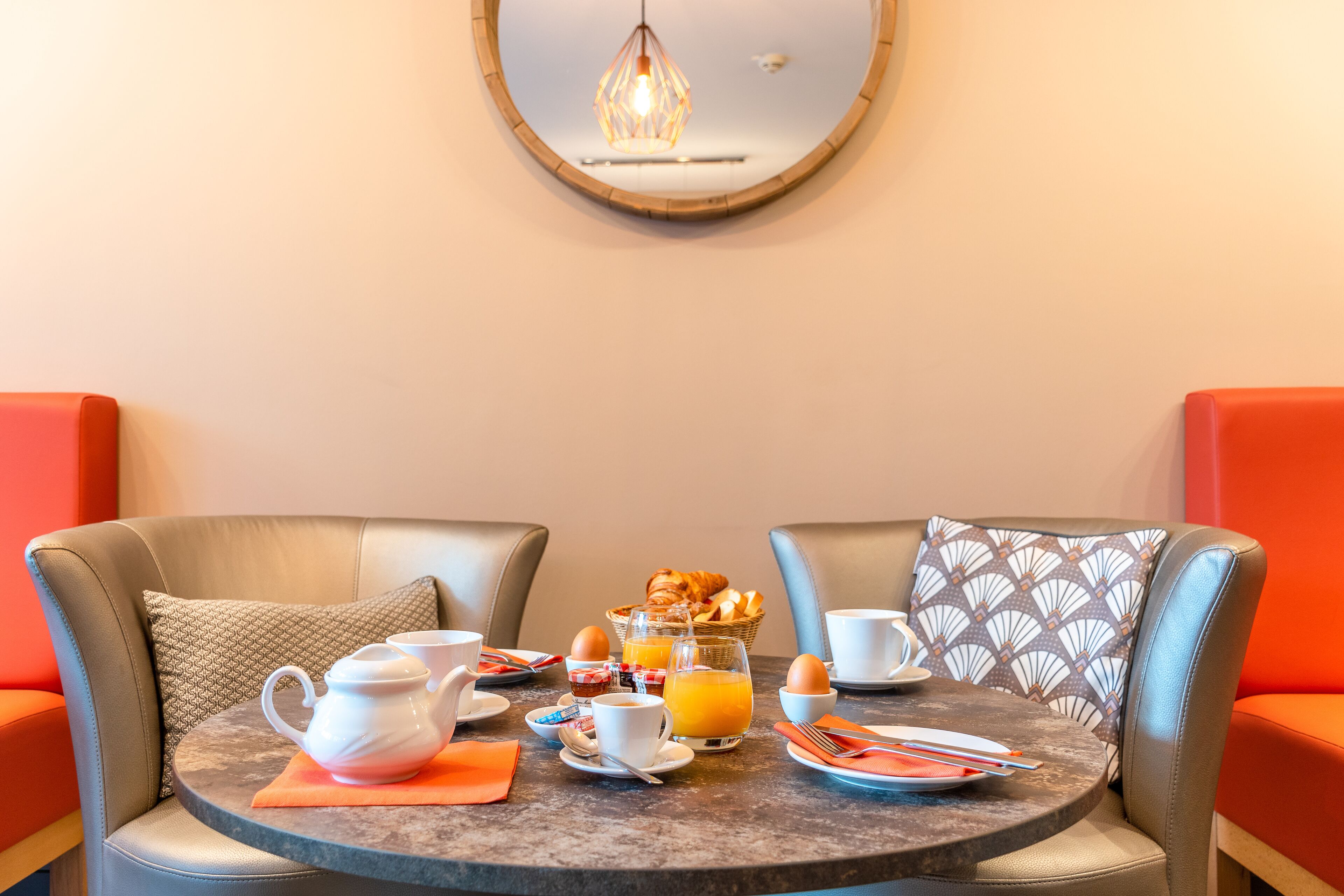 Ein Frühstückstisch mit Teekanne, Tassen und Croissants in einem Raum mit Ledersesseln und einem Spiegel an der Wand.
