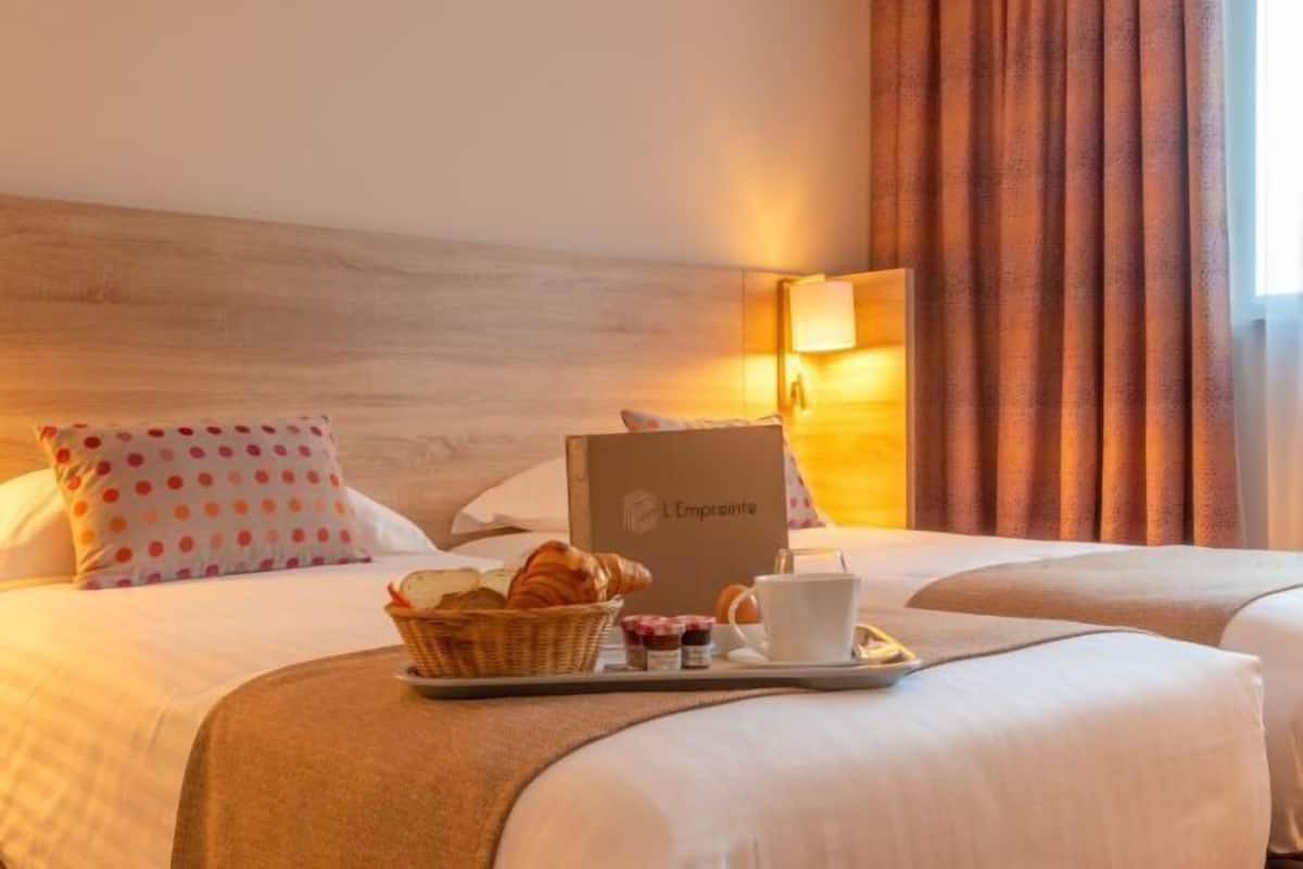 Una habitación de hotel con dos camas, una bandeja de desayuno con cruasanes, una cesta y una taza de café.