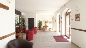 Zona de recepción con mostrador, sillas rojas, plantas en macetas y una mesa de madera.