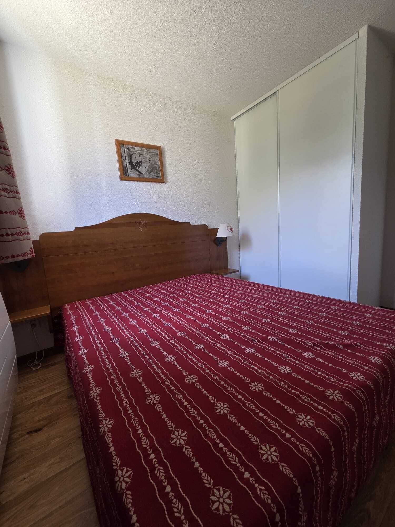 Una camera da letto con testiera in legno, copripiumino rosso a motivi decorativi, una cornice con un'immagine appesa al muro e un armadio bianco.