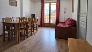 A room with a wooden dining table and chairs, a sofa, a bed, and a sliding glass door leading to an outdoor area. - VVF Résidence Albiez-Montrond Maurienne (Albiez-Montrond)
