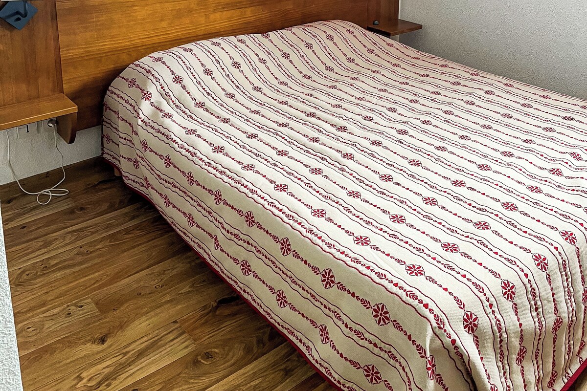Una cama individual con edredón estampado, cabecera de madera, lámparas de noche y mesita de noche de madera.