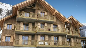 Un edificio de madera de varios pisos con balcones, probablemente un hotel o una cabaña, con montañas al fondo.