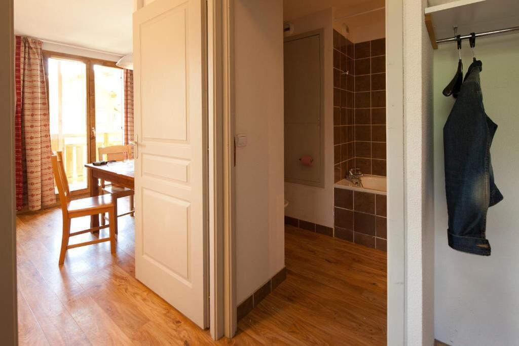 A room with a wooden floor, a white door, a shower area with tiled walls, and a hanging towel.
