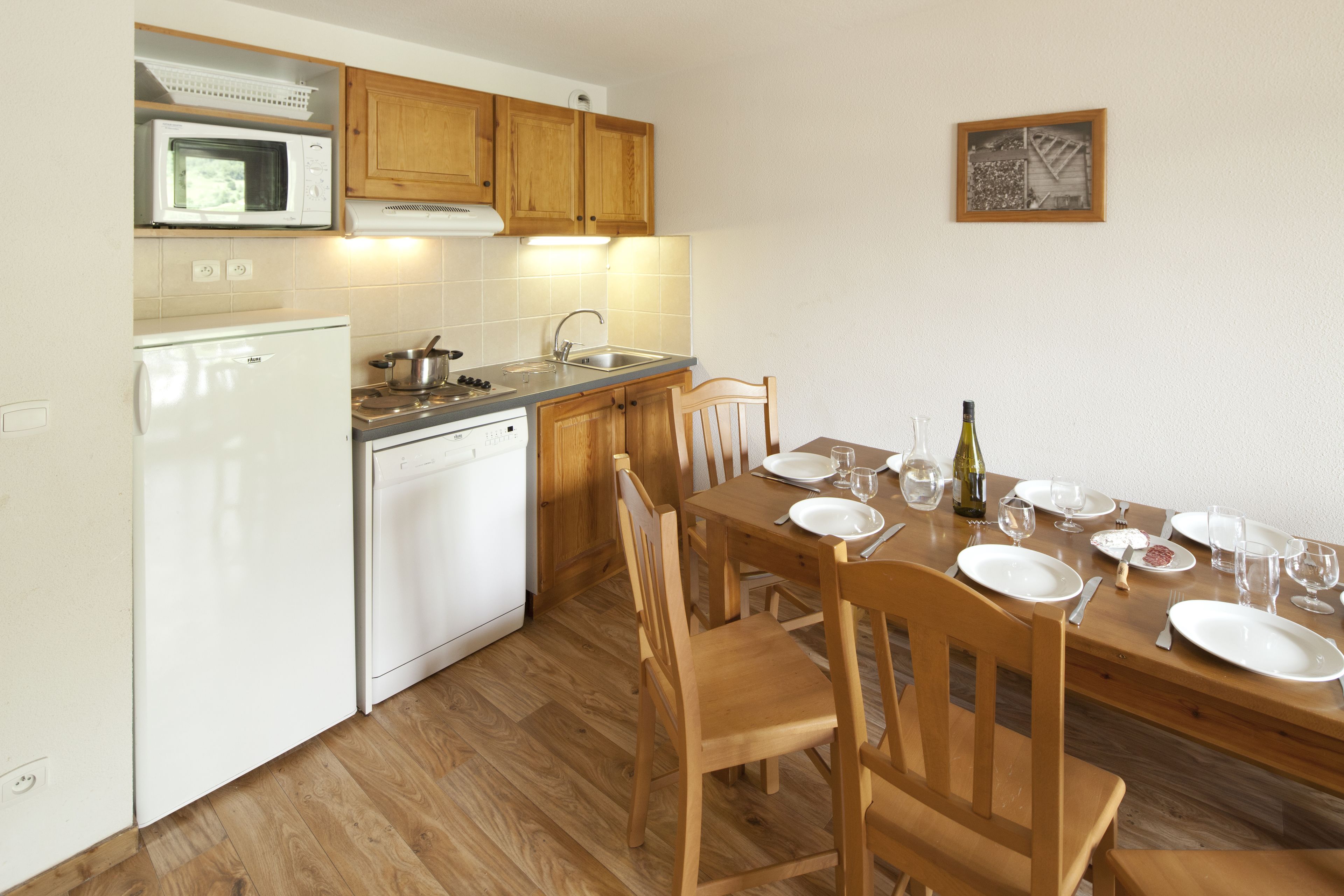 A kitchen with wooden cabinets, a microwave, a dishwasher, and a dining table set for four with plates, glasses, and cutlery.