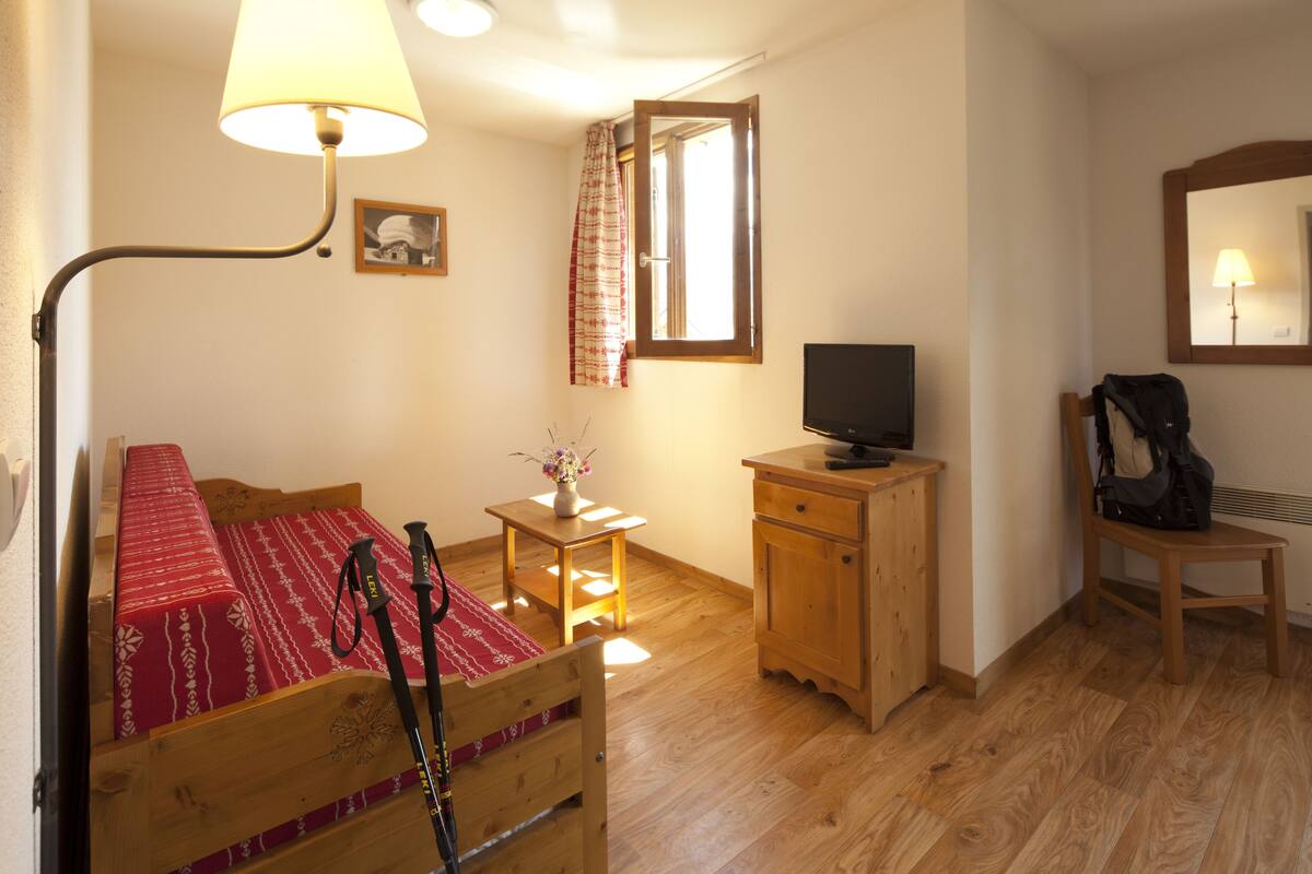 Una habitación pequeña con una cama individual, un escritorio de madera, televisión y espejo.