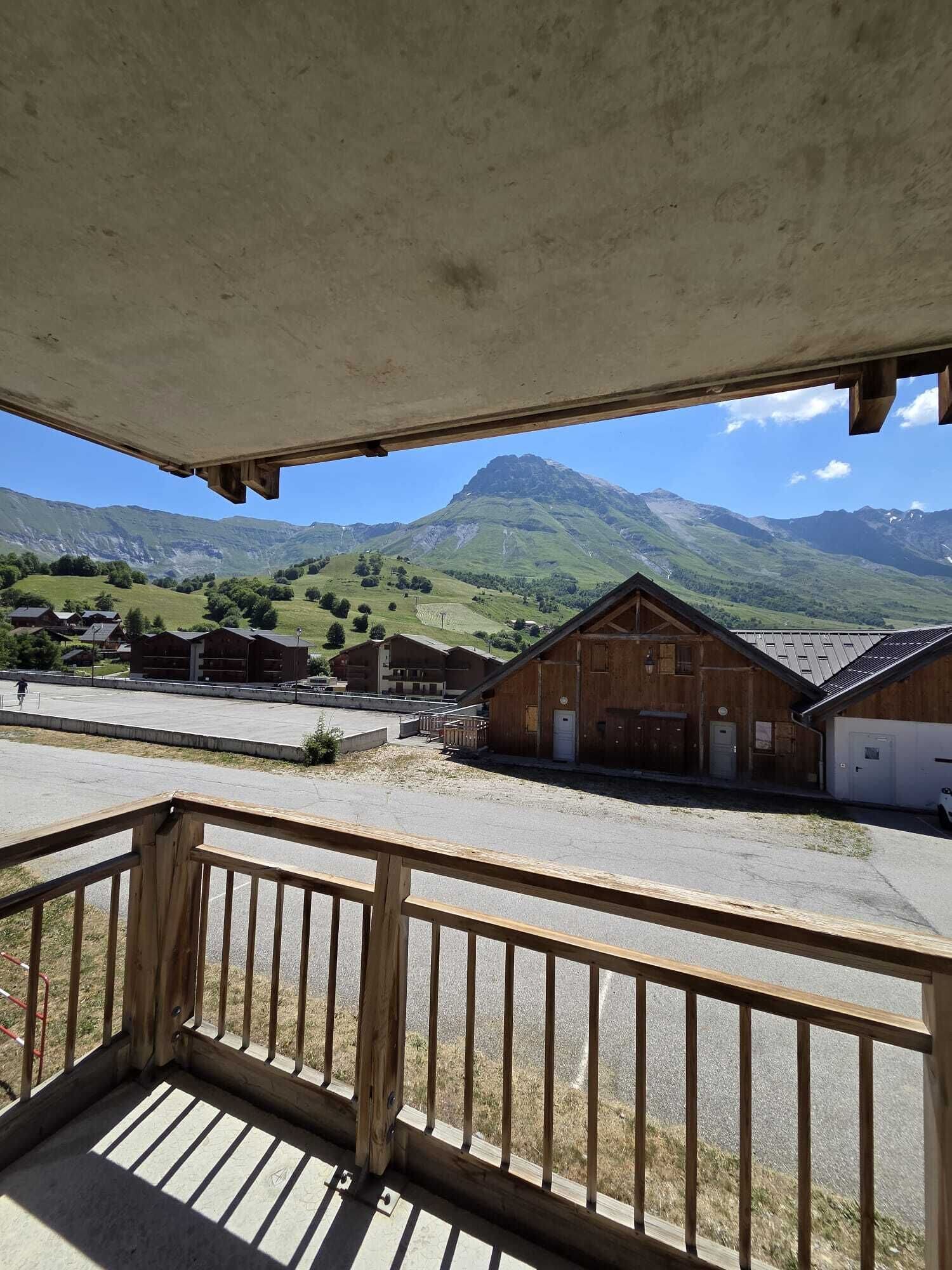 Un bâtiment en bois doté d’un balcon, d’un espace de stationnement et, en arrière-plan, d’un paysage montagneux.