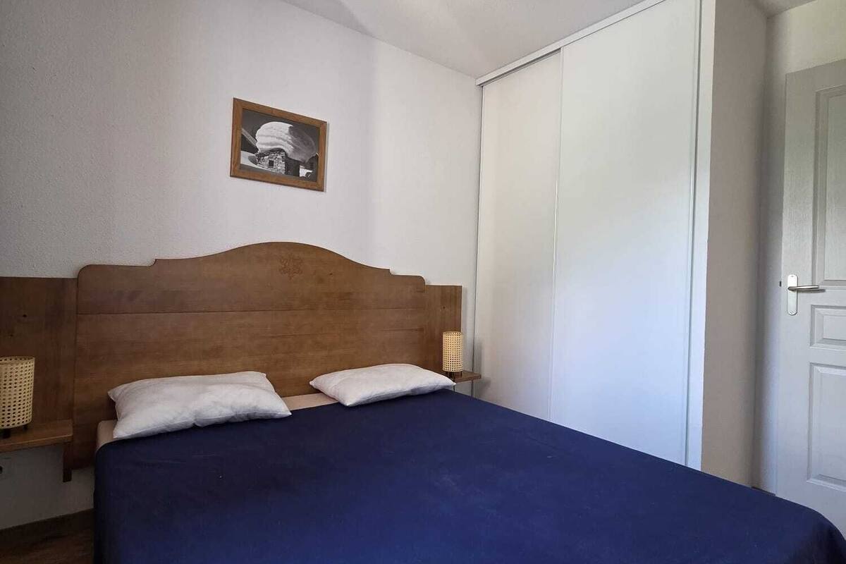 Una habitación con cama, cabecero, mesita de noche, lámpara, un cuadro en la pared y un armario.