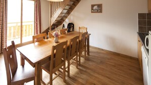 Un área de comedor con una mesa y sillas de madera, un florero con flores y una escalera que lleva a un balcón.